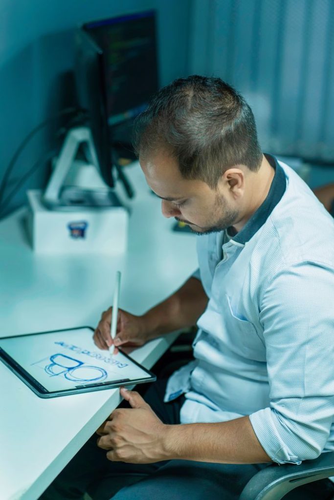 Focused man using a digital tablet for sketching while seated in a modern office environment.