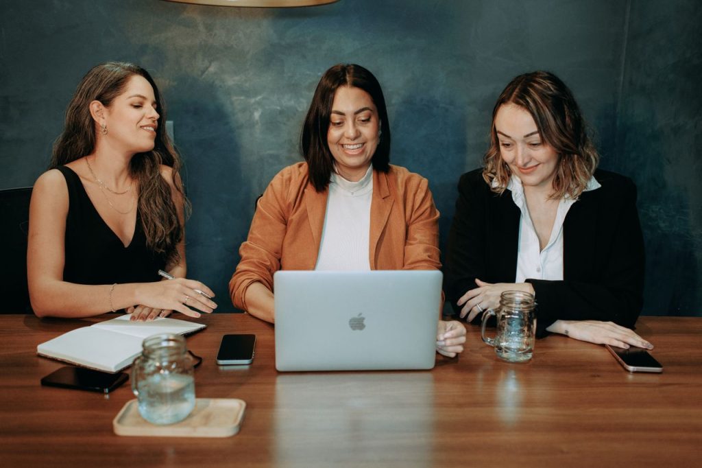 Three women engaged in a business meeting around a laptop, showcasing teamwork and collaboration.